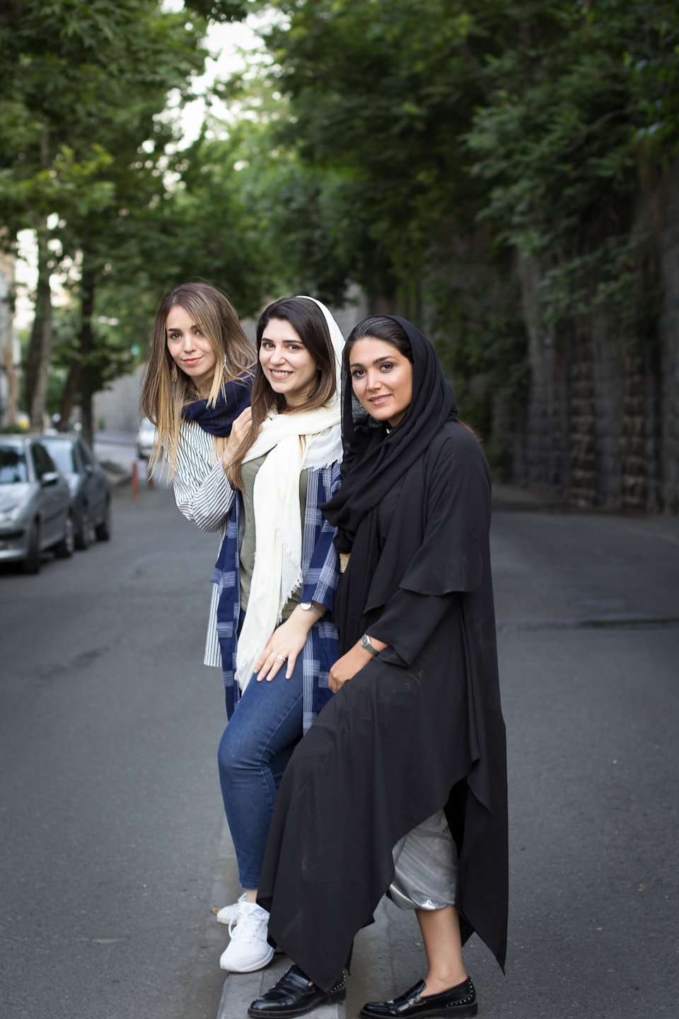 Three women smile while standing together on an urban street.