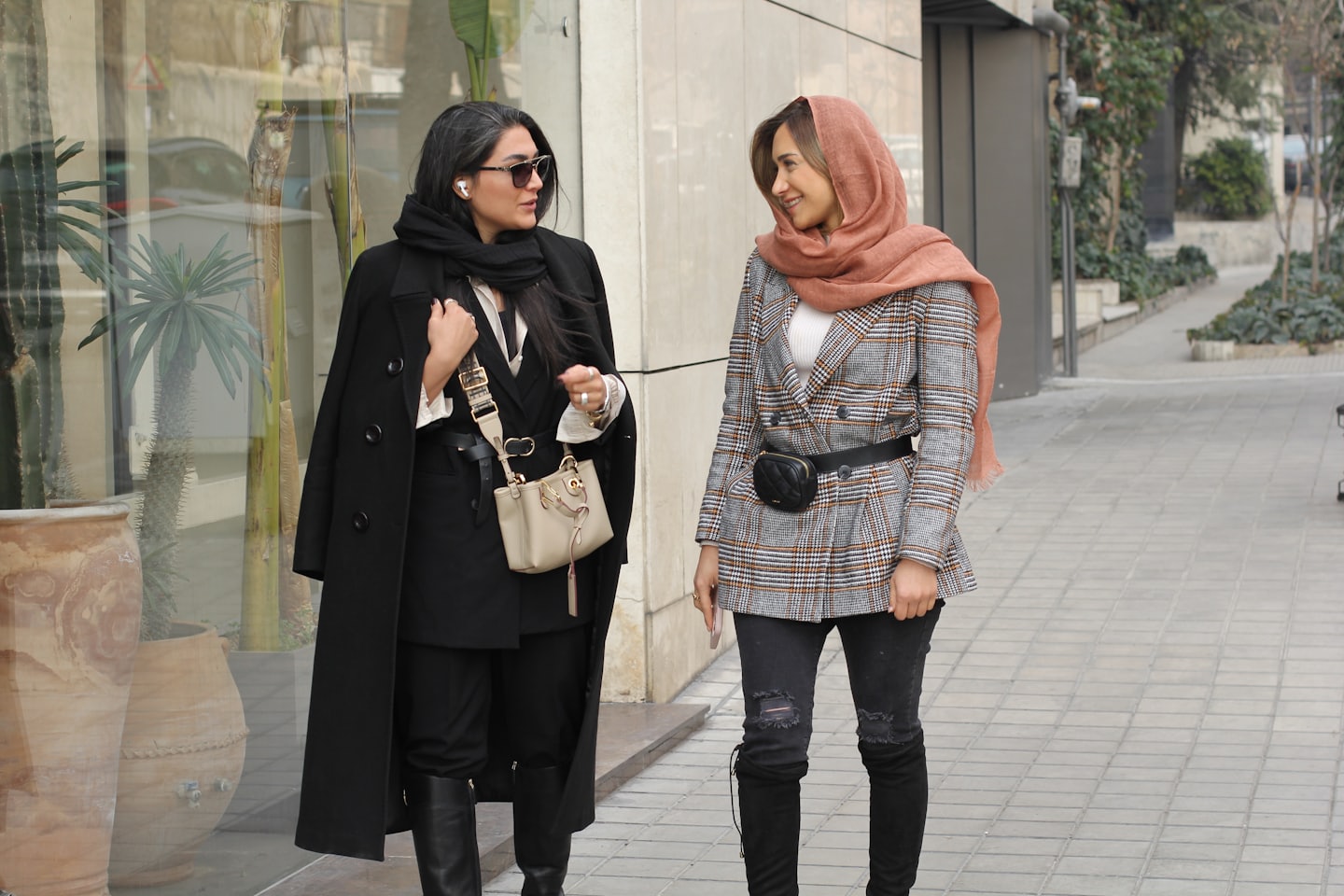 Two women walk and chat on a city sidewalk.